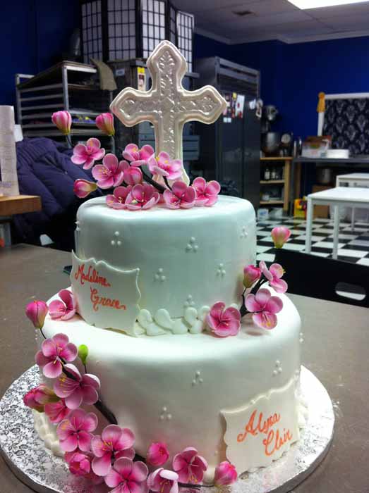 Light green 2-tiered cake with white cross on top and pink flowers